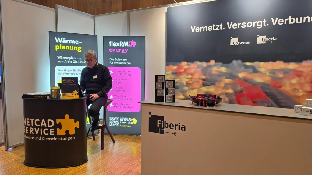 Messestand von NetCAD Service Aufstellern zu flexRM energy, Wärmeplanung und Glasfaser sowie einem Mitarbeiter am Beratungstisch.